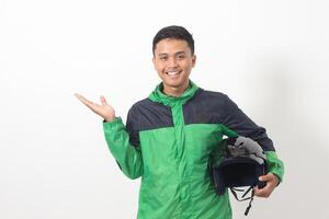 Portrait of Asian online taxi driver wearing green standing against white background, smiling and looking at camera, holding his helmet on the side photo