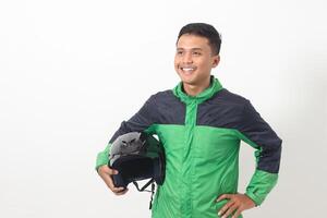Portrait of Asian online taxi driver wearing green standing against white background, smiling and looking at camera, holding his helmet on the side photo