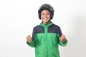 Portrait of Asian online taxi driver wearing green jacket and helmet raising his fist, celebrating success. Isolated image on white background photo