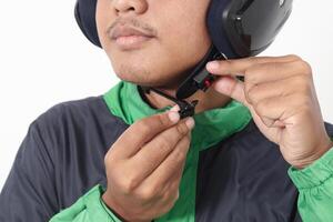 Close up portrait of Asian online taxi driver wearing green jacket and helmet demonstrating how to wear helmet correctly. Isolated image on white background photo