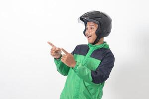 Portrait of Asian online taxi driver wearing green jacket and helmet pointing at empty space with finger. Isolated image on white background photo