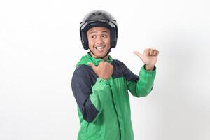 Portrait of Asian online taxi driver wearing green jacket and helmet pointing at empty space with finger. Isolated image on white background photo