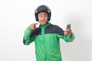 Portrait of Asian online taxi driver wearing green jacket and helmet holding mobile phone while pointing to the side. Isolated image on white background photo