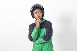 Portrait of Asian online taxi driver wearing green jacket and helmet thinking about question with hand on chin. Isolated image on white background photo