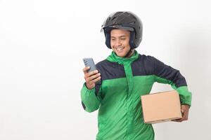 Portrait of Asian online courier driver wearing green jacket and helmet delivering package and box for customer while using mobile phone and taking order. Isolated image on white background photo