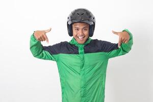 Portrait of Asian online taxi driver wearing green jacket and helmet pointing at empty space with finger. Isolated image on white background photo