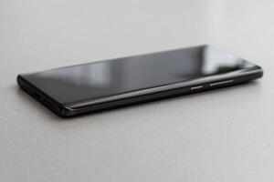 Black modern mobile phone with blank screen on black stone table background. Smartphone on old dark grey vintage texture background. photo