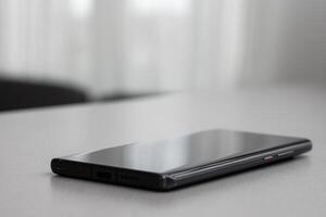 Black modern mobile phone with blank screen on black stone table background. Smartphone on old dark grey vintage texture background. photo
