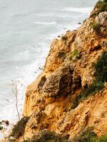 Steep, rugged cliffs overlooking the ocean, with textured rock formations and sparse vegetation photo