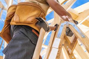 Construction Worker Using a Wooden Ladder to Build a Structure Under a Clear Blue Sky photo