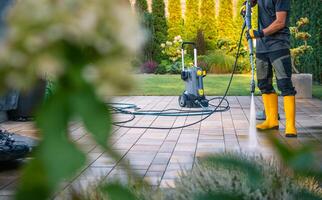Man Cleaning Patio Tiles With a Pressure Washer in a Well-Maintained Garden on a Sunny Day photo