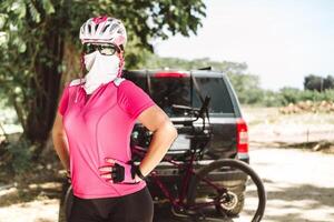 portrait of a woman with sportswear for cyclists, with helmet and glasses in the background her bicycle. adventure concept. photo