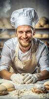 A smiling chef wearing a white hat and apron is standing in front of a table with dough. photo
