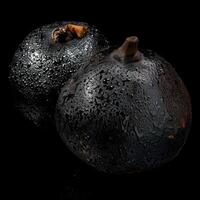 Two black fruits sit on a black surface photo