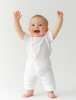 A baby in white shirt and pants standing with his hands up photo