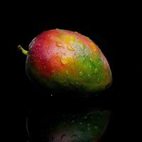 A mango is reflected in a black surface photo