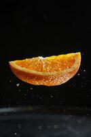 A slice of orange is falling into a bowl of water photo