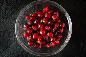 A bowl of red cranberries on a black surface photo