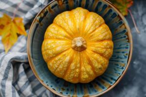 A yellow pumpkin in a blue bowl on a table photo