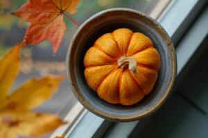 A small pumpkin sitting in a bowl on a window sill photo
