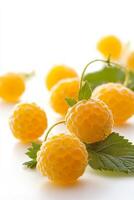 A group of yellow raspberries with leaves on a white surface photo