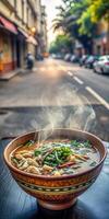 There is a bowl of soup on a table in an outdoor restaurant. The steam from the soup rises into the air, creating a cozy and welcoming atmosphere. photo