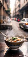 There is a bowl of soup on a table in an outdoor restaurant. The steam from the soup rises into the air, creating a cozy and welcoming atmosphere. photo