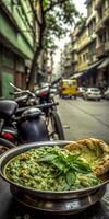 A bowl of food with green herbs sits on a table in front of a motorcycle. The scene is set in a city street with cars and a truck in the background photo