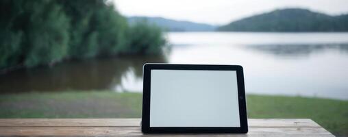 Tablet pc with blank screen on wooden table near lake photo