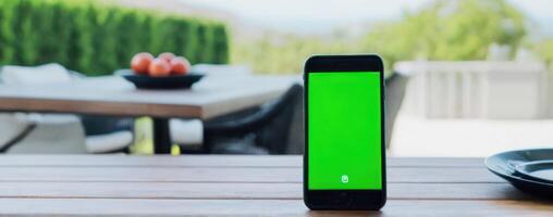 An iphone with a green screen sitting on top of an outdoor table photo