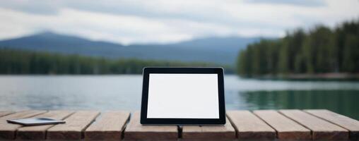 Tablet pc with blank screen on wooden table near lake photo