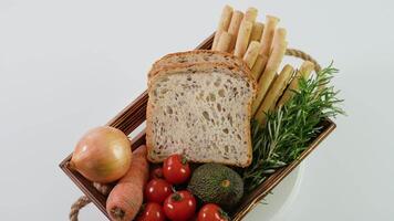 Wooden basket with fresh vegetables, cheese bread sticks and fresh toaster bread rotate on white video