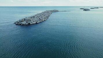 Rocky breakwater extending into calm blue waters. A serene image of a rocky breakwater extending into calm blue waters. video