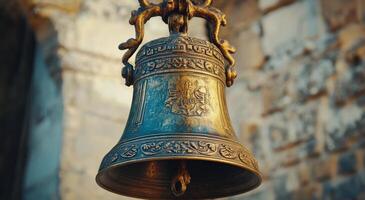 An ornate bell hangs from a stone wall, reflecting sunlight on a warm afternoon photo