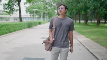 Slow-motion Male student walking with laptop and bag in the park, working online, He is walking in nature to relax from work and study, studying online, modern tech concept. video
