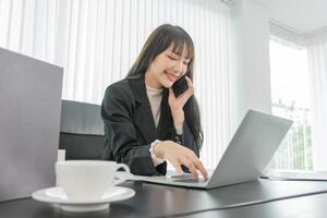 woman talking on the mobile phone and smiling while sitting at her working place in office. photo