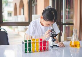 little scientist looking through a microscope and test tubes filled with chemicals for learning about science and experiments. photo