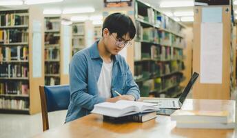 Male college students are working on laptops and searching for books to study, make reports, find useful information in college room. Concept of reading, learning and intelligence. photo