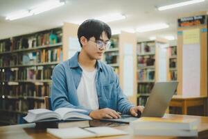Male college students are working on laptops and searching for books to study, make reports, find useful information in college room. Concept of reading, learning and intelligence. photo