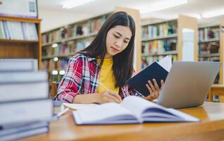 Female college student working on laptop and searching for books to study, make report, find useful information in college room. Concept of reading, learning and intelligence. photo