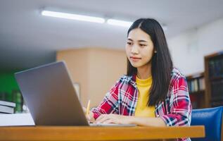 Female college student working on laptop and searching for books to study, make report, find useful information in college room. Concept of reading, learning and intelligence. photo