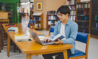 Male college students are working on laptops and searching for books to study, make reports, find useful information in college room. Concept of reading, learning and intelligence. photo