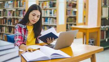 Female college student working on laptop and searching for books to study, make report, find useful information in college room. Concept of reading, learning and intelligence. photo