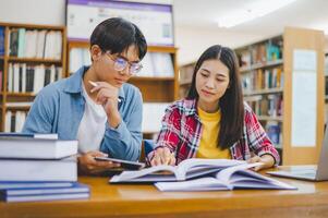 Students are consulting each other working on laptops and searching for books to study, make reports, find useful information in university room. Concept of reading, learning and intelligence. photo