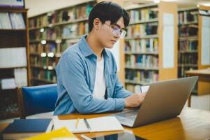 Male college students are working on laptops and searching for books to study, make reports, find useful information in college room. Concept of reading, learning and intelligence. photo