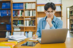 Male college students are working on laptops and searching for books to study, make reports, find useful information in college room. Concept of reading, learning and intelligence. photo