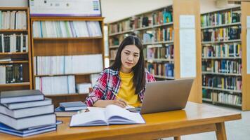 Female college student working on laptop and searching for books to study, make report, find useful information in college room. Concept of reading, learning and intelligence. photo