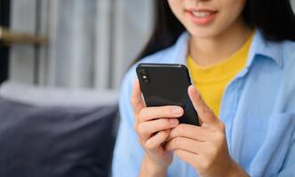 Smiling young asian woman using mobile phone checking social media,app playing game, shopping online, ordering delivery relax while sitting on a couch at home with laptop computer photo