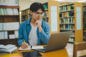 Male college students are working on laptops and searching for books to study, make reports, find useful information in college room. Concept of reading, learning and intelligence. photo