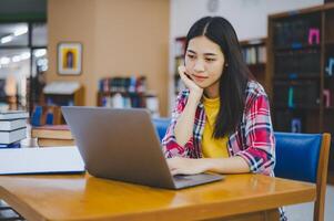Female college student working on laptop and searching for books to study, make report, find useful information in college room. Concept of reading, learning and intelligence. photo